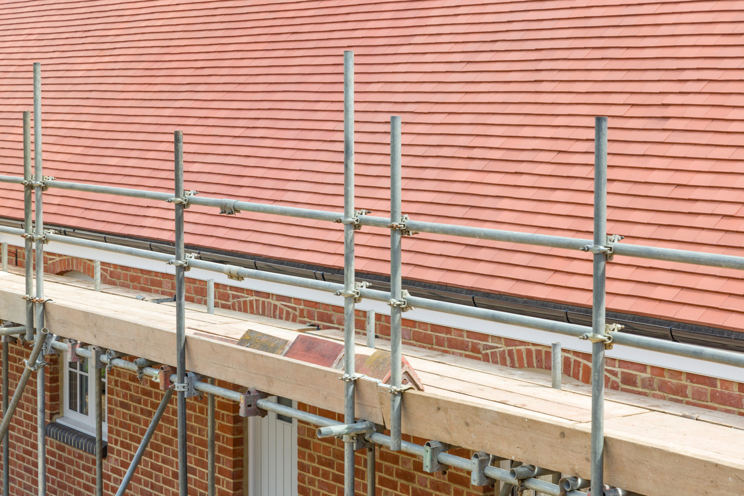 Scaffolding is set up alongside a brick building with a tiled roof, suggesting construction or maintenance work in progress.